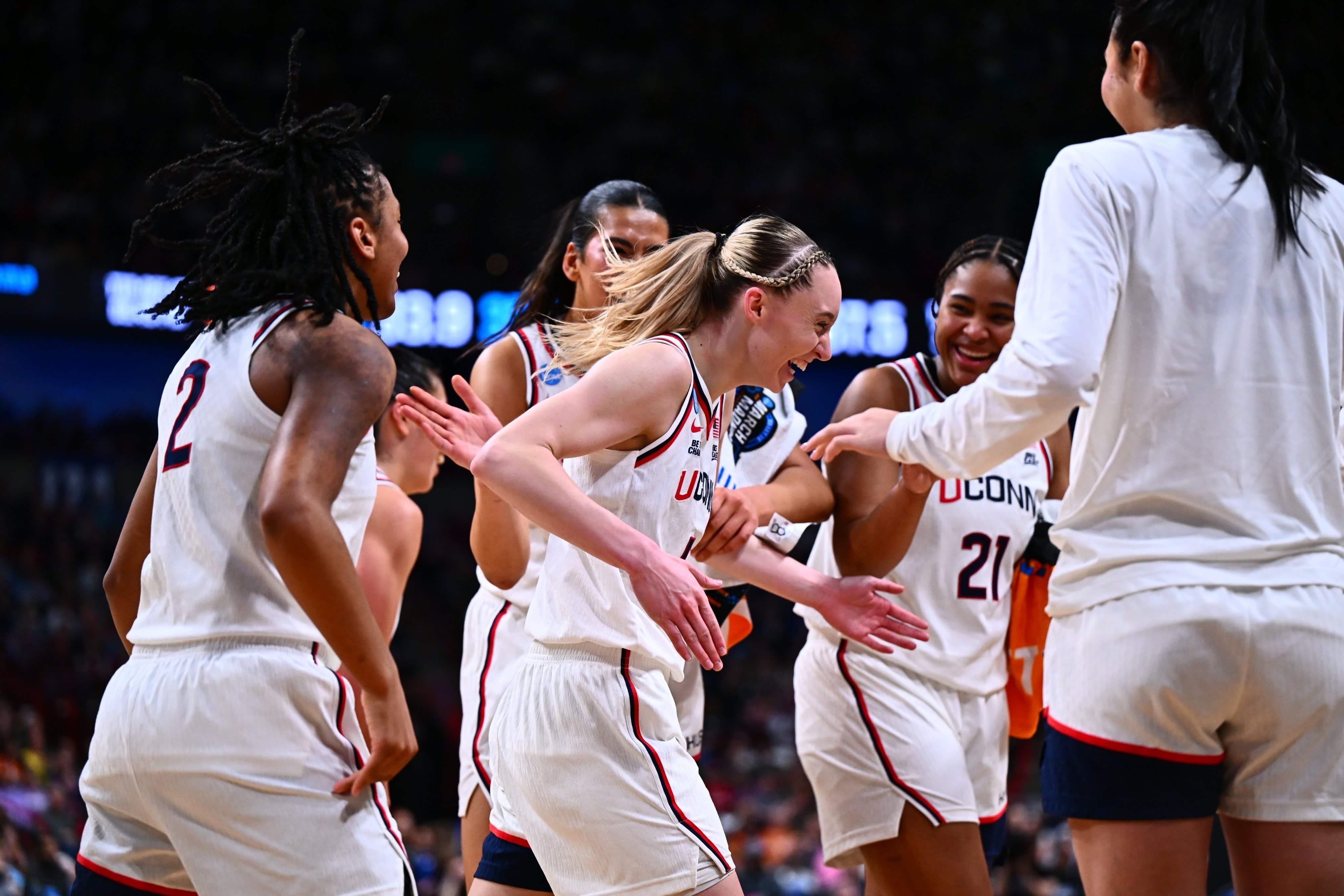 A women's basketball player cheers while surrounded by teammates.